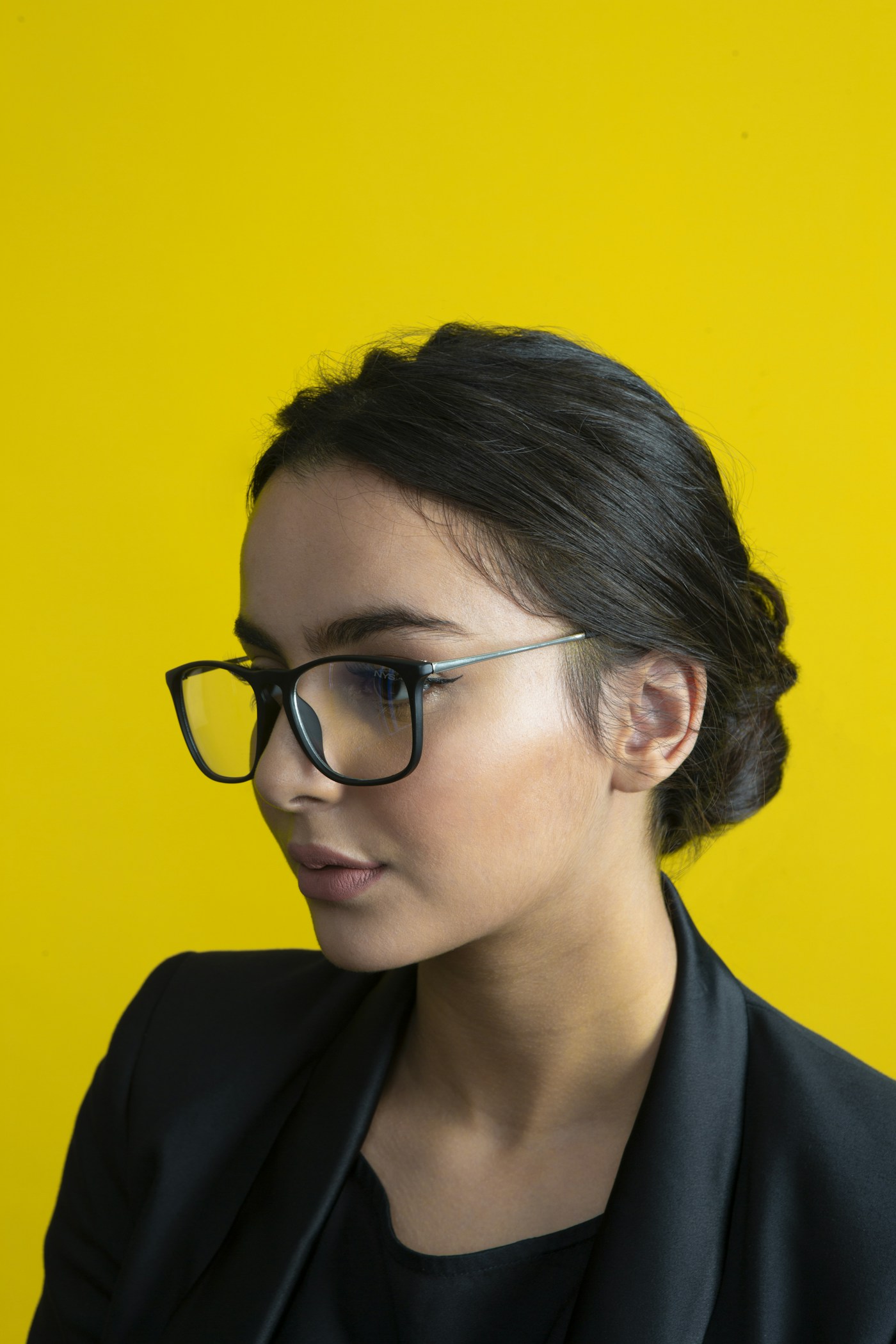 Retrato de una mujer con lentes sobre fondo amarillo; fotografía referencial